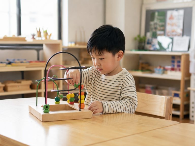 child playing wooden maze toy on table in preschool classroom with natural light