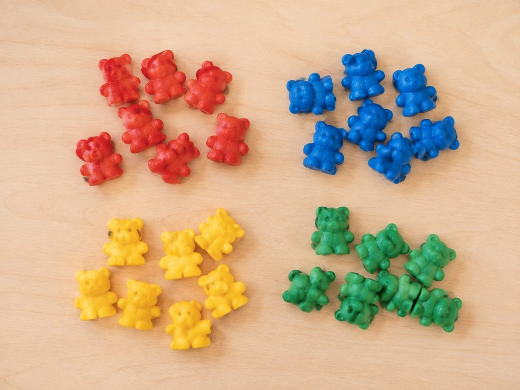 Colorful counting bear manipulatives sorted by color on a wooden table, used as hands-on math learning toys for 3 year olds in preschool classrooms