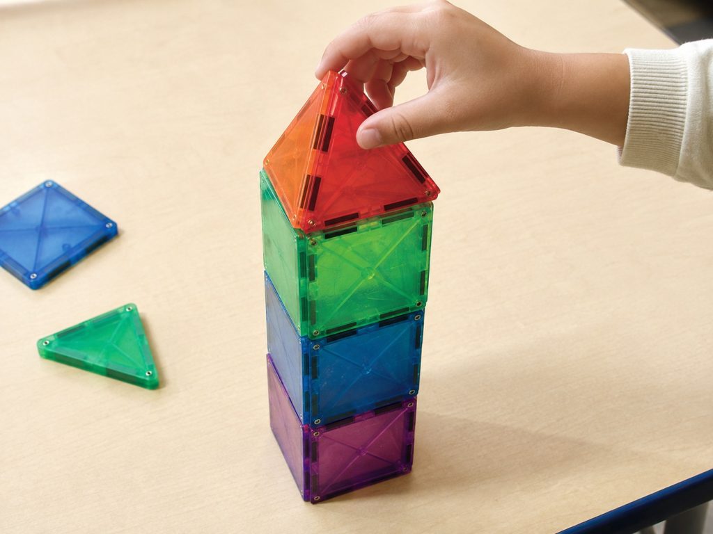 child building a tower with magnetic geometric tiles, developing spatial reasoning and STEM skills through hands-on preschool play