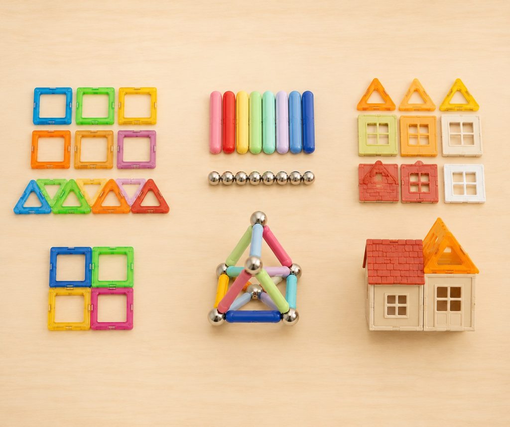 three common formats of magnetic building toys laid side by side: flat geometric tiles, rods and spheres, and themed construction sets
