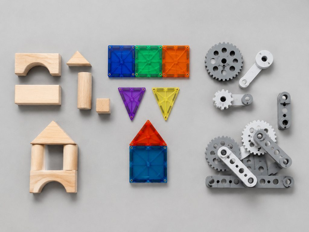 Flat lay of three types of Vindstier construction toys: wooden blocks, magnetic tiles, and gear linkage kits
